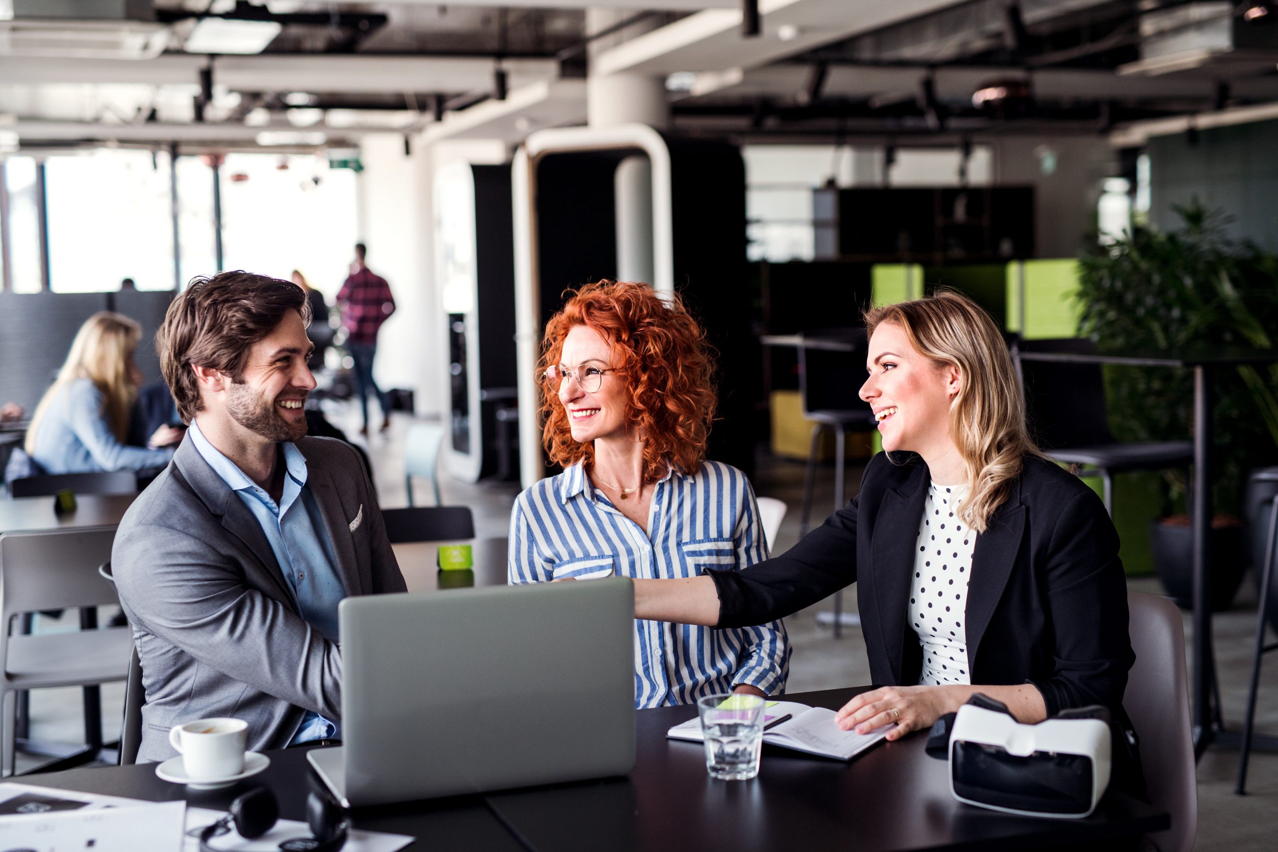 A group of young business people with laptop sitting in an office, talking.